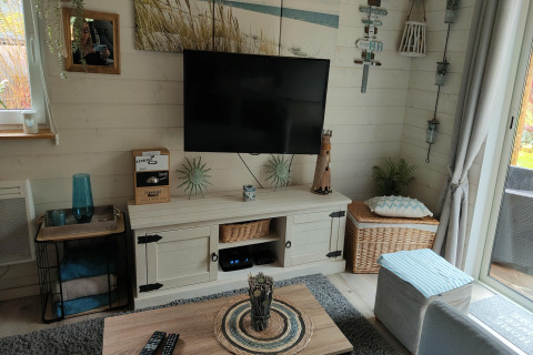 Gezellige woonkamer in lodge Chatillon 67 in België met tv aan de muur, rustieke decoratie en lichtinval.