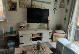 Gezellige woonkamer in lodge Chatillon 67 in België met tv aan de muur, rustieke decoratie en lichtinval.