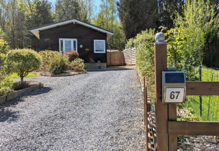 Oprit van grind naar lodge Chatillon 67 in België, houten huisje met veel groen en voorjaarszon.