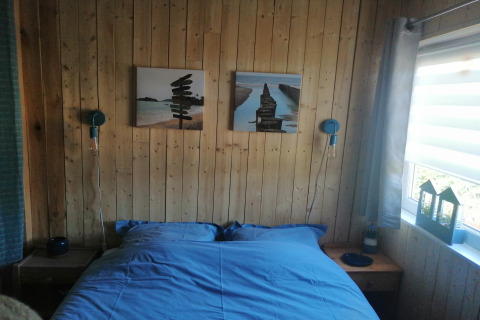 Slaapkamer in lodge Chatillon 67 in België met houten wanden, blauw beddengoed en daglicht.