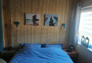 Slaapkamer in lodge Chatillon 67 in België met houten wanden, blauw beddengoed en daglicht.