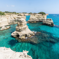 Klippen und türkisfarbenes Wasser nahe Lacona in der Toskana, Italien, unter klarem, sonnigem Himmel.