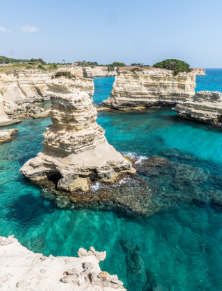 Formaciones rocosas y aguas turquesas cerca de Lacona, Toscana, Italia, bajo un cielo despejado y soleado.