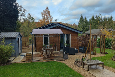 Sfeervolle lodge ‘Chatillon 67’ in België met houten terras, tuinmeubelen en een groene omgeving.