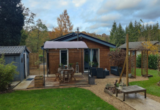 Sfeervolle lodge ‘Chatillon 67’ in België met houten terras, tuinmeubelen en een groene omgeving.