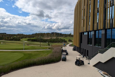 Uitzicht vanaf Chatillon 67 lodge in België met golfkarretjes, groene velden en een modern gebouw.