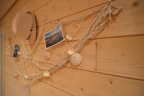 Wanddecoratie met net, schelpen, foto’s en een hoed aan een houten muur in Chatillon 67, België.