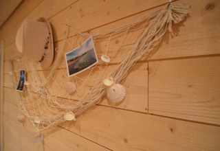 Wanddecoratie met net, schelpen, foto’s en een hoed aan een houten muur in Chatillon 67, België.