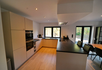 Cucina moderna nello Chalet DES BOIS in Belgio con pavimento in legno, piani neri e grandi finestre.