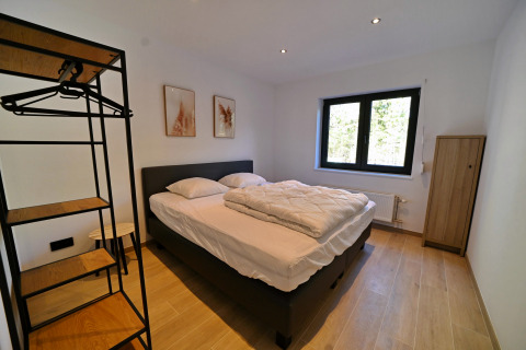 Moderne soveværelse på Chalet «DES BOIS» i Belgien med dobbelt seng, tøjstativ og stort vindue.