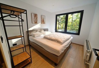Camera moderna allo Chalet «DES BOIS» in Belgio con letto grande, guardaroba aperto e finestra sulla foresta.