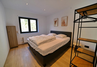Moderne soveværelse på Chalet «DES BOIS» i Belgien, dobbeltseng, åbent skab, store vinduer.