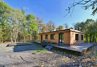 Moderne træhytte Chalet «DES BOIS» i Belgien omgivet af skov, med stor terrasse og picnicbord.