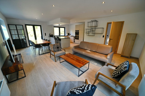 Moderne opholdsstue og køkken i Chalet «DES BOIS», Belgien, med stilfuld indretning og åbent rum.
