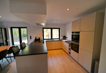 Cucina moderna nello Chalet «DES BOIS» in Belgio con pavimento in legno, piano nero e grandi finestre.