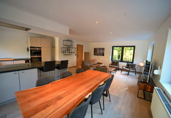 Zona giorno e pranzo moderna presso lo Chalet «DES BOIS» in Belgio con cucina a vista e ampie finestre.