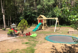 Parco giochi all'aperto in un glamping con altalene, scivolo, tappeto elastico e casetta tra gli alberi.