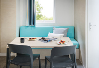 Eethoek in chalet ‘Vlaamse gaai’ in België met blauwe bank, tafel, ontbijtborden en stoelen.