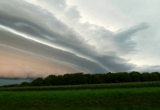 Ciel dramatique avec couches nuageuses au-dessus d’un champ vert près d’un hébergement glamping.