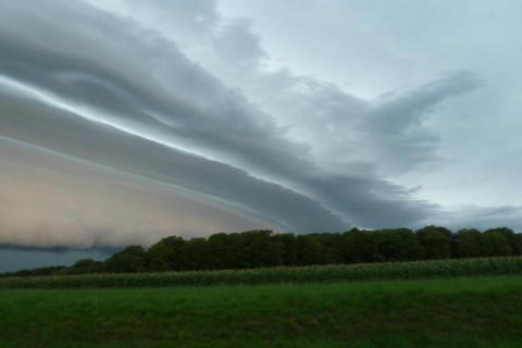 Dramatisk himmel over grøn mark og træer ved glamping-ophold, med lagdelte skyer i horisonten.