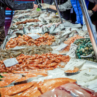 Puesto de mercado con pescado y mariscos frescos sobre hielo, clientes comprando productos.