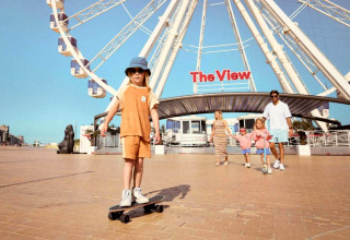 Gezin geniet van een zonnige dag aan het reuzenrad 'The View', kind rijdt op een skateboard.