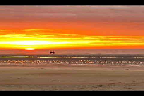 Glamping sulla spiaggia con un tramonto spettacolare e due persone che passeggiano lungo la riva.