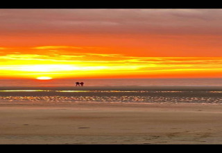 Glamping-oplevelse ved stranden med en spektakulær solnedgang og to personer der nyder udsigten.