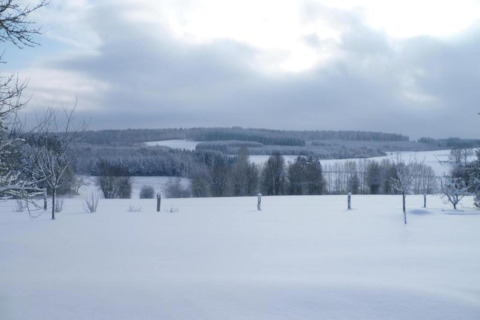 Vista invernale da una sistemazione glamping, con campi, alberi e colline innevati sotto un cielo nuvoloso.