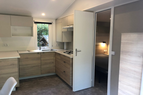 Cuisine moderne du chalet Goudhaantje en Belgique avec placards en bois clair et vue sur la chambre.