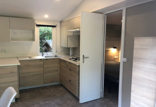 Cuisine moderne du chalet Goudhaantje en Belgique avec placards en bois clair et vue sur la chambre.