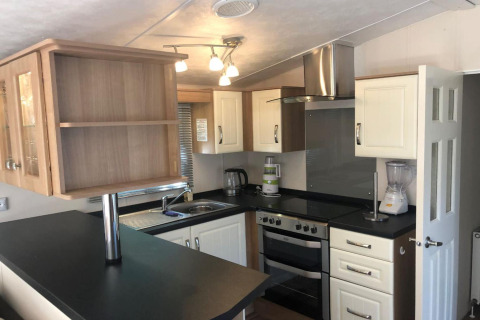 Cucina moderna con piani neri, mobili bianchi, fornello, frullatore e cappa in uno chalet in Belgio.