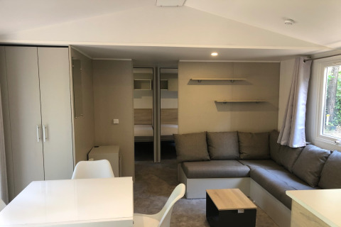 Interiør af chalet 'Goudhaantje' i Belgien med komfortabel sofa, spisebord, skabe og udsigt til skov.