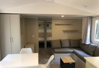 Interiør af chalet 'Goudhaantje' i Belgien med komfortabel sofa, spisebord, skabe og udsigt til skov.