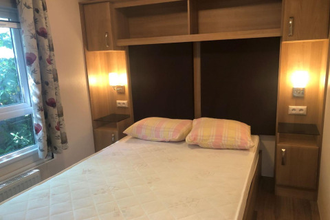 Chambre au chalet Koperwiek en Belgique avec lit double, tables de nuit, placards et rideaux fleuris.