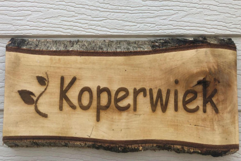 Insegna di legno con la scritta 'Koperwiek' e motivo a foglia, fotografata in uno chalet in Belgio.