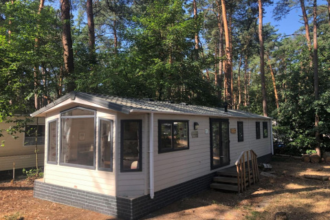 Chalet chiamato 'Koperwiek' in Belgio, circondato da alberi alti e bosco, in una giornata di sole.