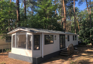 Chalet chiamato 'Koperwiek' in Belgio, circondato da alberi alti e bosco, in una giornata di sole.