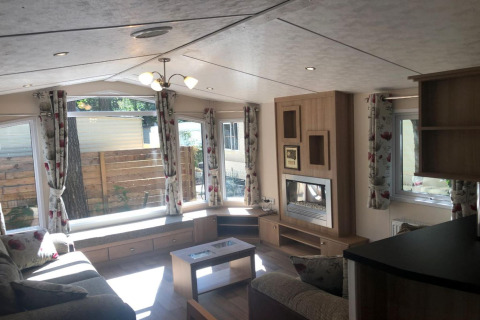 Intérieur du chalet Koperwiek en Belgique, avec grandes fenêtres, rideaux fleuris et salon chaleureux.