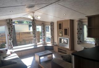 Interno dello chalet Koperwiek in Belgio con ampie finestre, tende floreali e soggiorno accogliente.