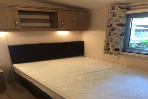 Chambre du chalet Koperwiek en Belgique avec lit double, armoire murale, fenêtre et rideau à fleurs.