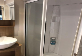 Salle de bain du chalet Koperwiek en Belgique avec douche moderne, lavabo blanc et étagère en bois