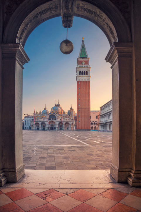 Vista a través de un arco hacia la Plaza de San Marcos en Venecia con la basílica y el campanario al amanecer.