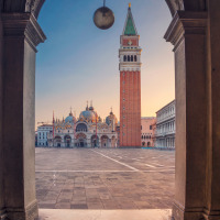 Vue à travers une arche sur la Place Saint-Marc à Venise avec basilique et campanile au lever du soleil.