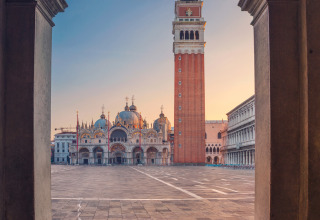 Vista a través de un arco hacia la Plaza de San Marcos en Venecia con la basílica y el campanario al amanecer.