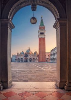 Vista a través de un arco hacia la Plaza de San Marcos en Venecia con la basílica y el campanario al amanecer.