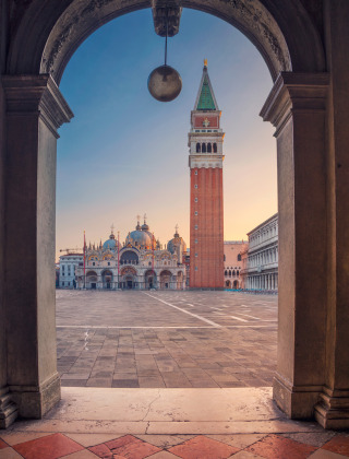 Vista a través de un arco hacia la Plaza de San Marcos en Venecia con la basílica y el campanario al amanecer.