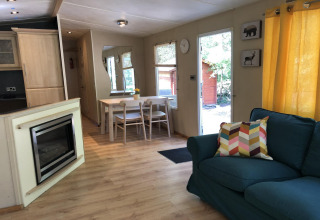 Lyst opholdsområde i lodge Bosuil i Belgien med spisebord, sofa, pejs og udsigt til have.