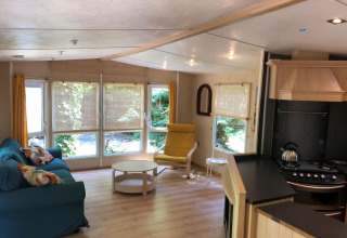Soggiorno della lodge Bosuil in Belgio con grandi finestre, divano, poltrona e cucina a vista.