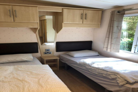 Soveværelse i lodge 'Bosuil' i Belgien med to enkeltsenge, vindue og skabe over sengegavle.